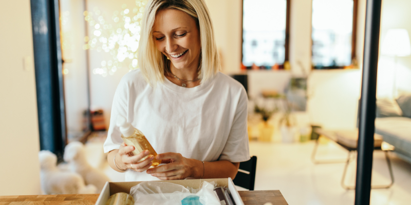 a blonde woman looking at a bottle from a subscription box in her home